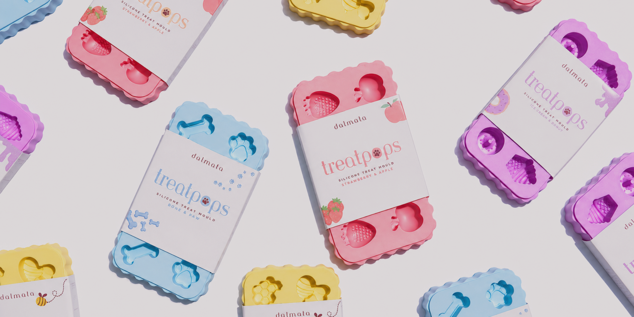 A styled flat-lay of several pastel-colored silicone dog treat pops molds in their retail packaging, arranged on a clean white background.